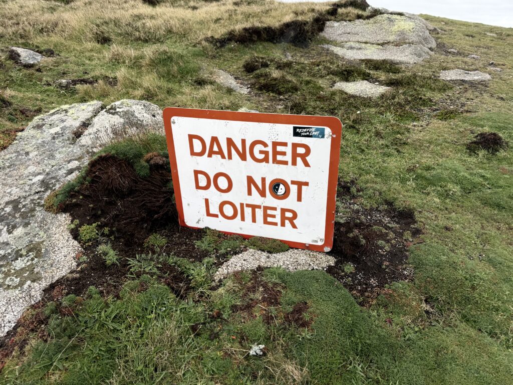 A sign reading DANGER DO NOT LOITER amongst some short grass and low granite rocks.